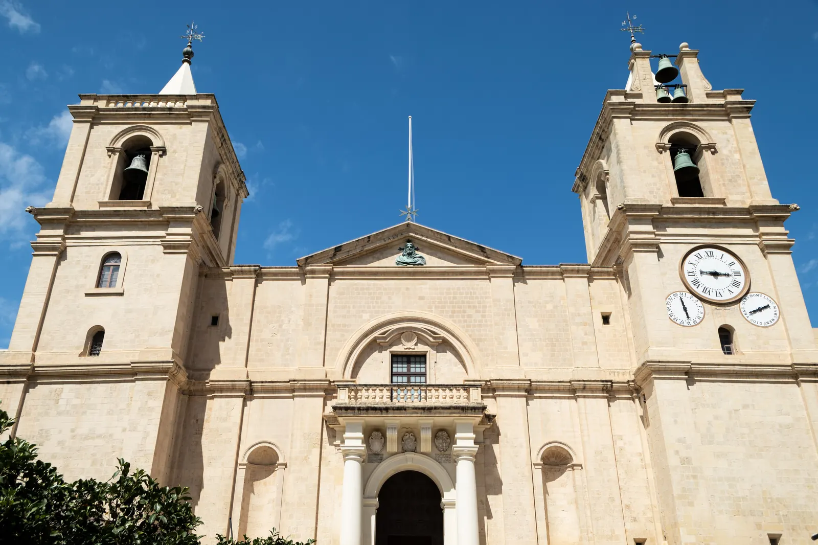 La sobria facciata in calcare della Concattedrale di San Giovanni a La Valletta, con due campanili e un balcone sopra il portale