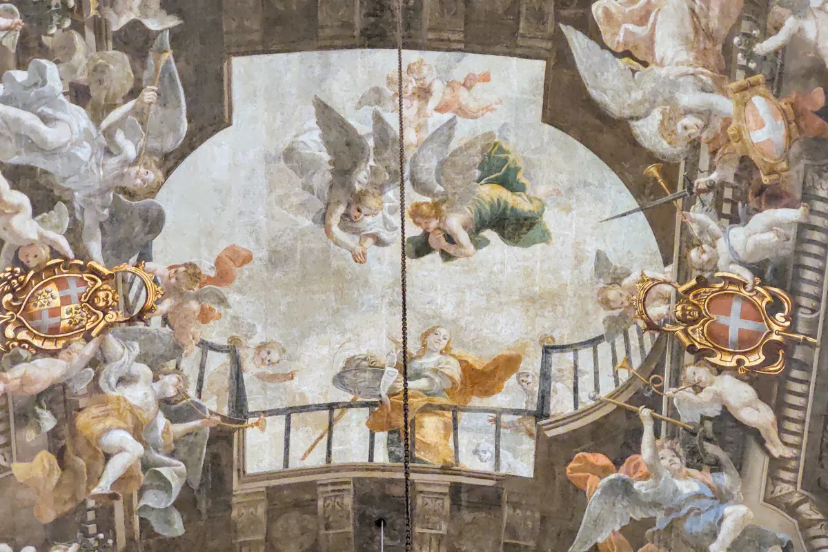 Un soffitto dipinto nella Concattedrale di San Giovanni, con angeli, trombe e cartigli dorati attorno a una scena ovale centrale