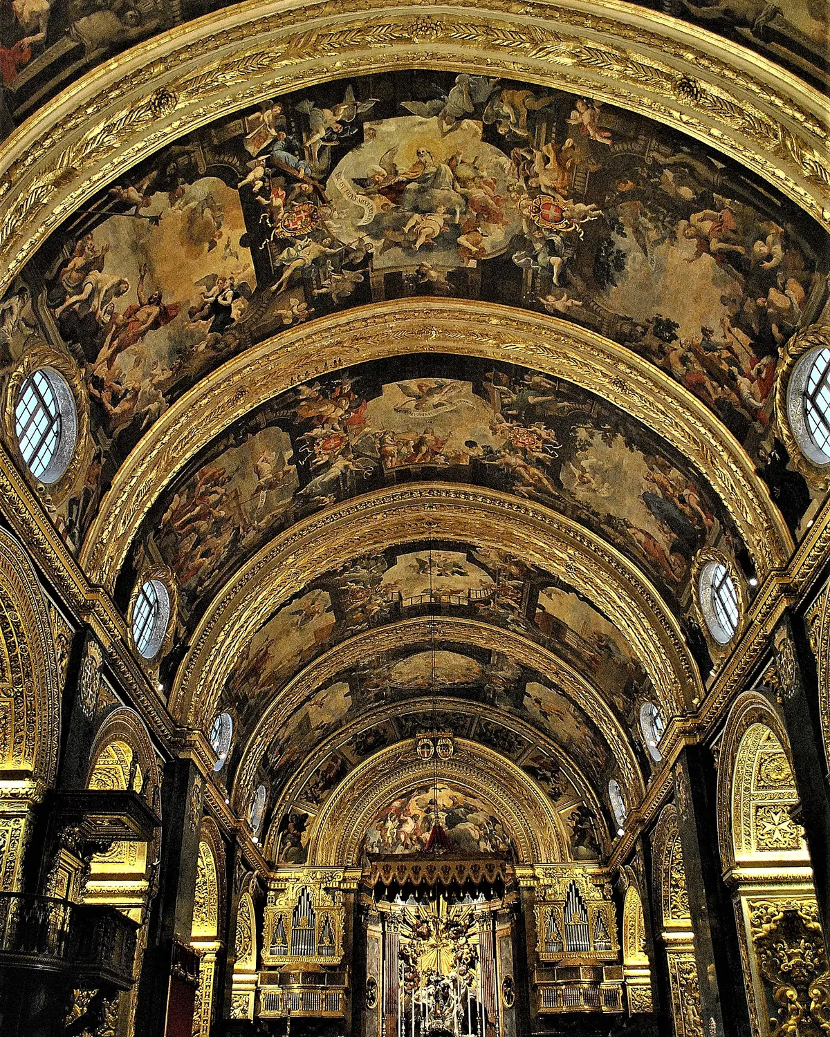 La volta a botte dipinta della Concattedrale di San Giovanni vista dal basso, con costoloni dorati che incorniciano scene della vita di San Giovanni Battista